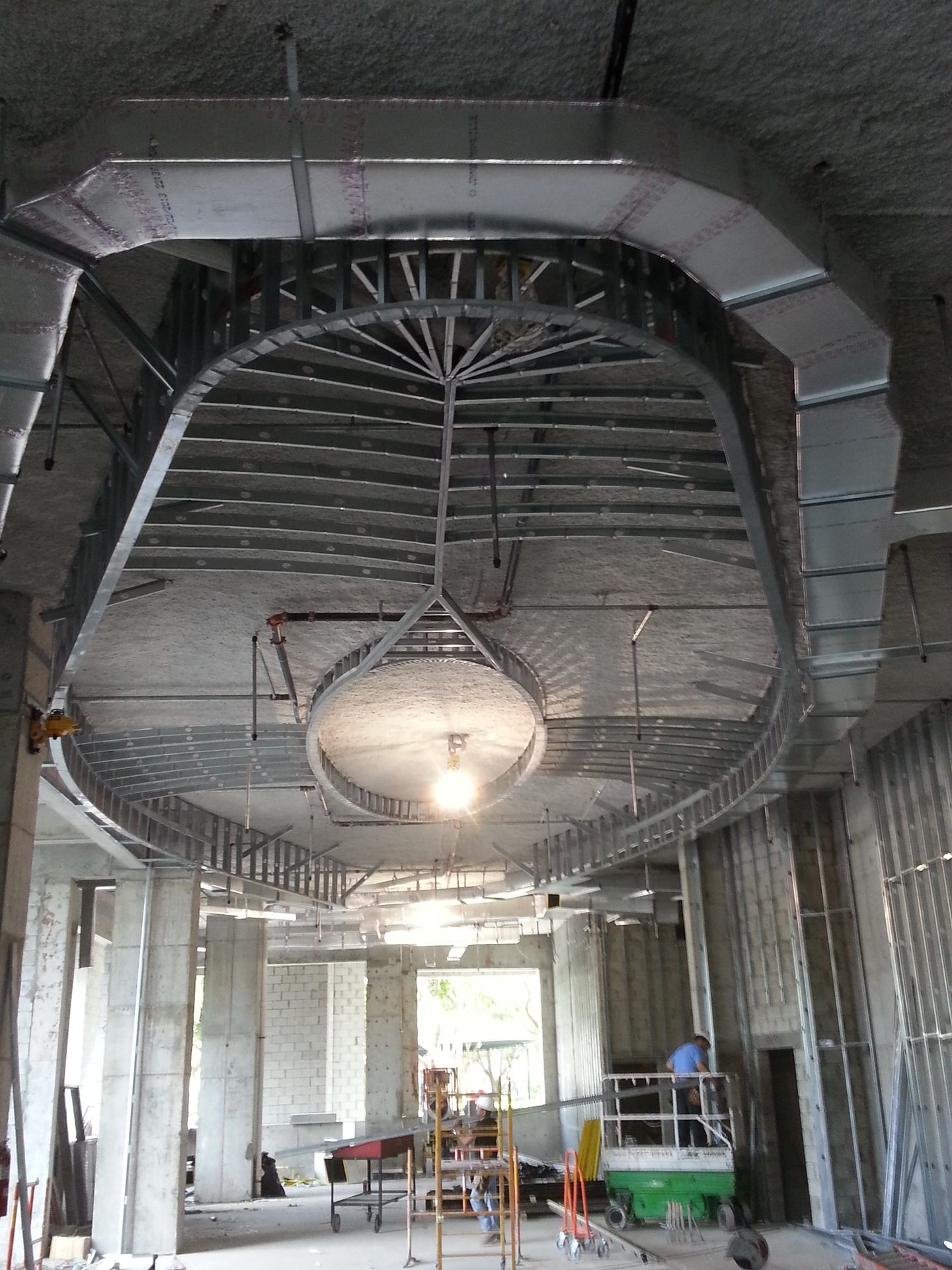 Interior of a construction site showing an intricate metal framework installed on the ceiling with workers present.